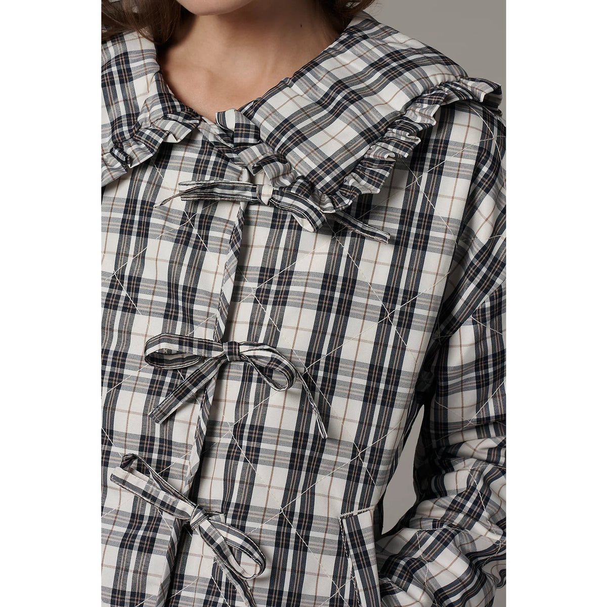 Quilted plaid jacket detail showing ruffled collar, tie closures, and stitched padding