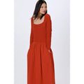 Rust red smocked midi dress with long sleeves, textured bodice, and scoop neckline.