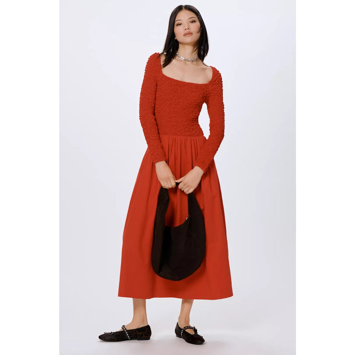 Rust red long-sleeve midi dress with textured bodice, gathered waist, and full skirt.