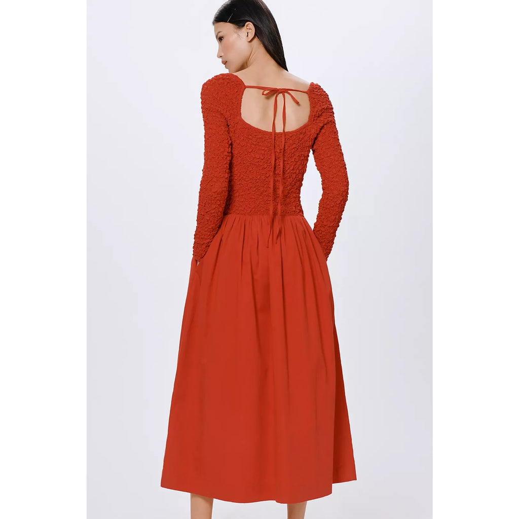 Back view of rust red long-sleeve midi dress with tie-back detail and gathered skirt.